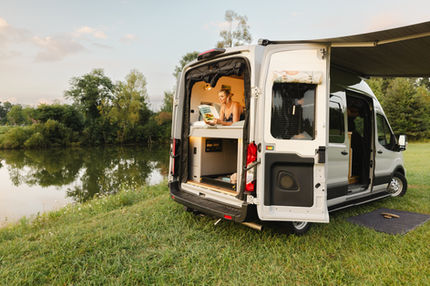 Camper van parked near water with awning extended.