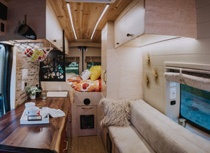 Camper van dining area with table, plant, and wood cabinetry.