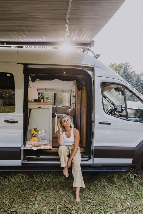 Young woman sitting at the open sliding door of a Drifter Vans Signature model camper van, enjoying a quiet moment and the open-air connection to nature.