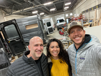 Friends playing frisbee near their parked camper van at a lakeside campground.