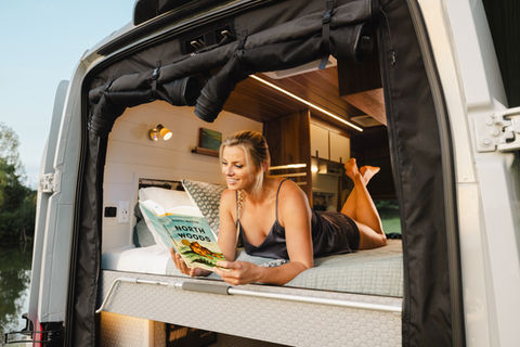 Person hiking near a camper van parked at a scenic trailhead, enjoying outdoor adventure.