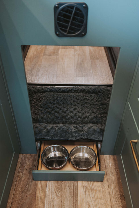 Custom built-in dog bed and food bowls integrated into the lower cabinetry of a Drifter Vans campervan interior