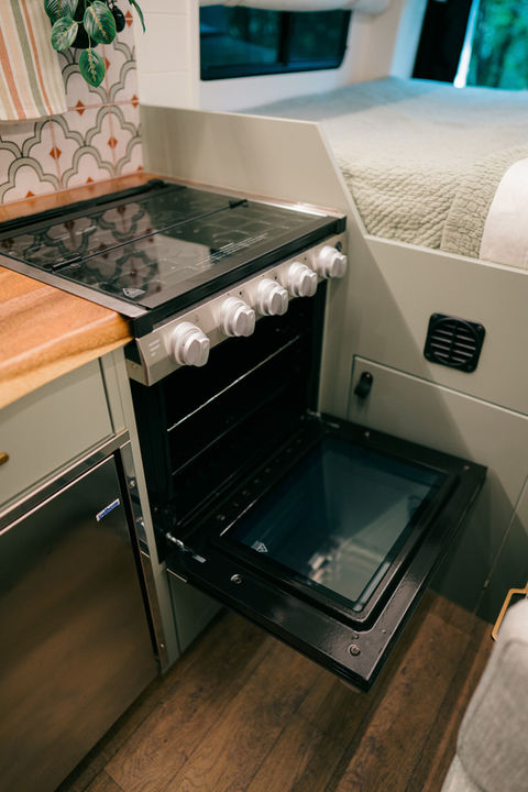 Camper van kitchen with oven open and wood flooring.
