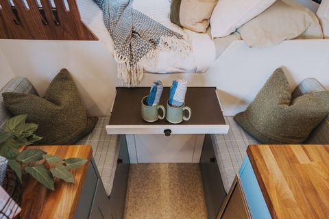 Camper van small pull-out table with mugs and pillows.