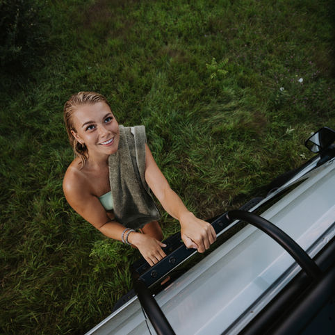 Woman climbing the ladder on her camper van to go sun bath on the roof rack