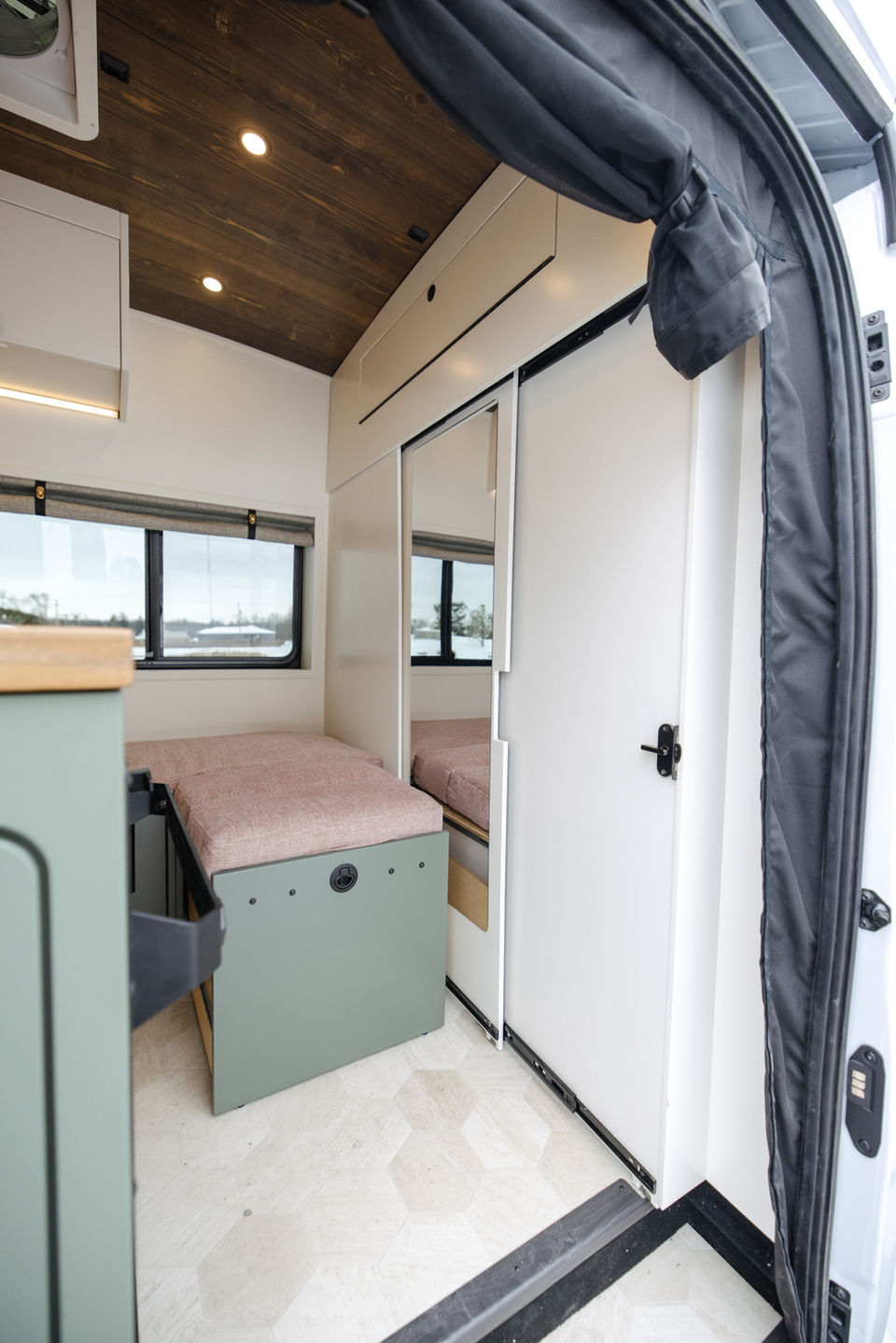 Camper van seating area with pink cushion and storage below.
