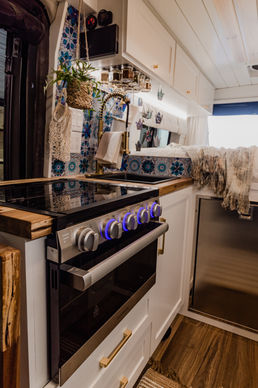 Camper van galley kitchen with wood countertops and modern appliances.