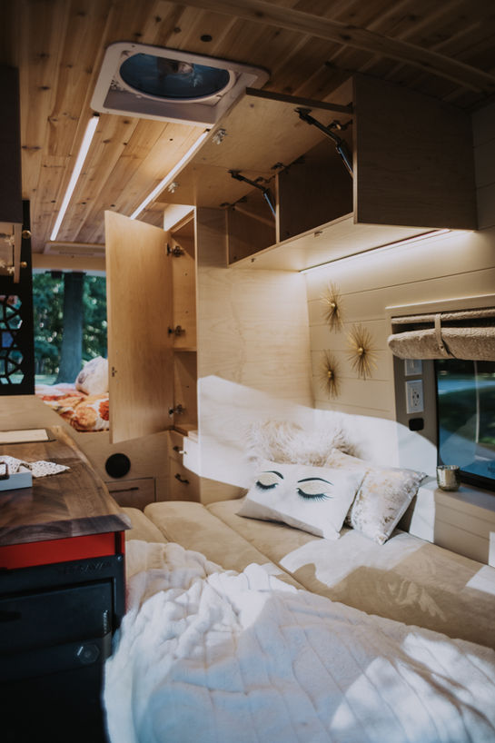 Camper van interior with wood ceiling and cozy sleeping area.