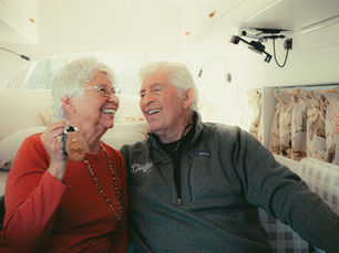 Smiling elderly couple sitting inside a cozy campervan, holding van keys and laughing together.