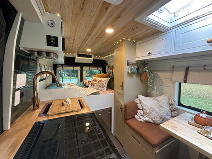 Camper van interior with wood ceiling, white cabinets, and kitchen area.