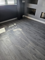 Grey wood-effect laminate flooring fitted in a modern living room with realistic wood grain finish.
