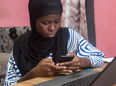 Young woman in hijab using a phone next to a laptop.