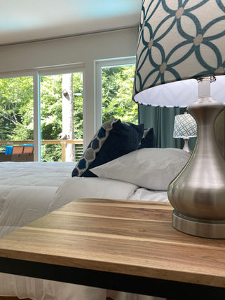 "Bright and airy master bedroom featuring high-end linens and large windows with lake, stream, and lush forest views".
