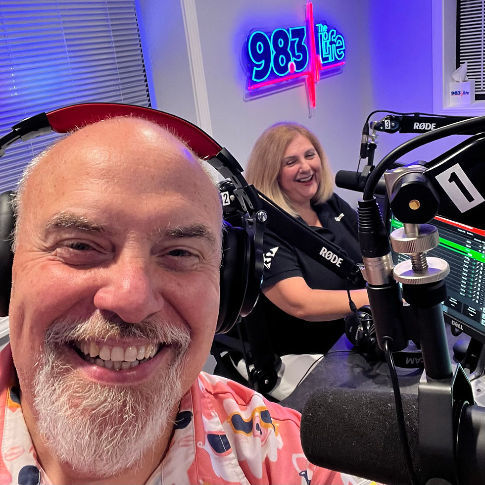 Marty Jalove, Master Happiness and Nonna Kofman, Signarama Grayslake smiling in a radio studio. A neon sign reads "98.3 The Life." They're wearing headphones and surrounded by microphones.
