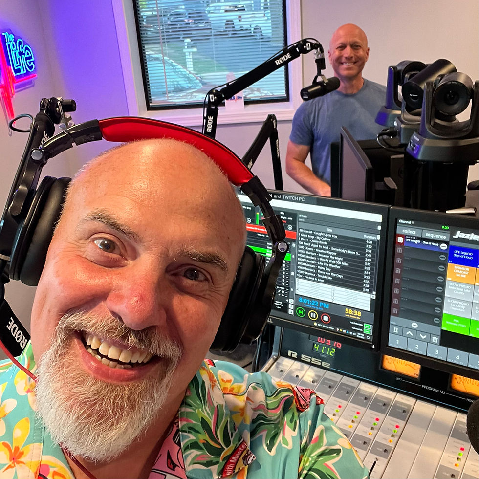 Marty Jalove, Master Happiness and Joe Janicki in a radio studio, one in a colorful shirt taking a selfie while smiling. Audio equipment and neon sign visible. Jovial mood.