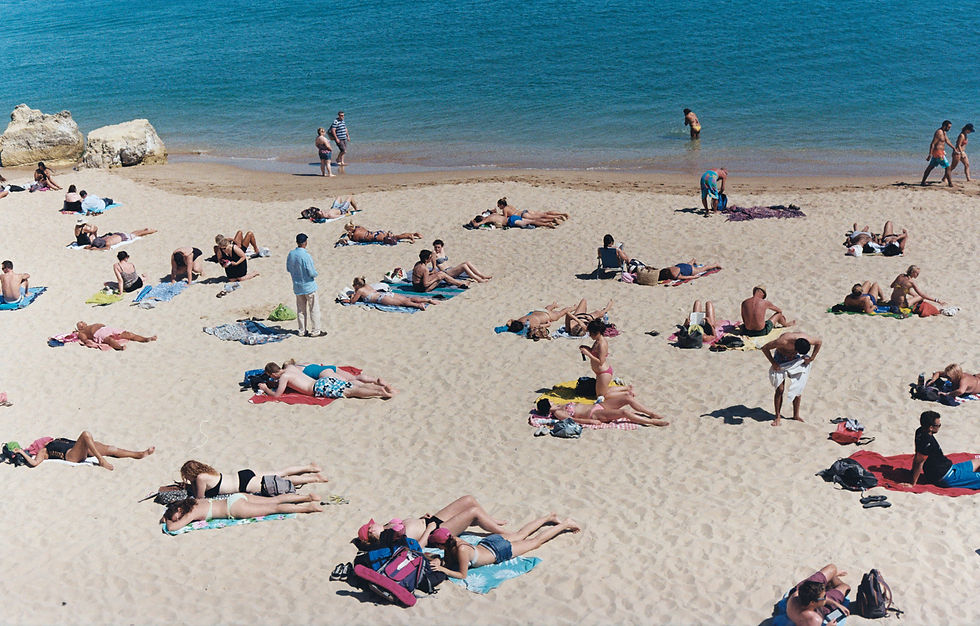 An eye-level shot reveals a busy beach on a sunny day. People dot the sandy shore, many sunbathing on colorful towels.