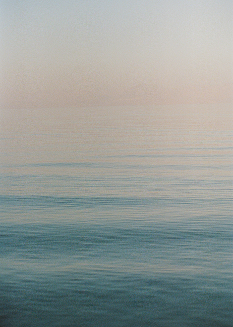 The image shows a serene seascape with gentle waves during the dawn. The sky transitions from a pale pink to a soft blue at the horizon.