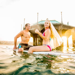 Unique engagement photo on the beach and in the sea. Bridal veil. Surf board. Hermosa Beach. Couple on a surfboard for engagement photos. Couple kissing for engagement photos. Engagement photographer Los Angeles GoShiggyGo Shiggy