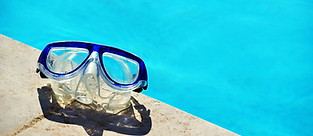 A pair of blue and clear goggles sitting on concrete on the side of a pool