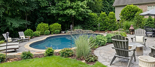 A backyard pool with two groups of patio furniture around the pool