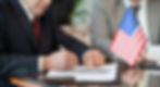 man signing document with american flag next to him