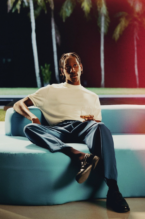 A man in blue slacks and a white shirt poses on a 70's style coach in a Miami house.