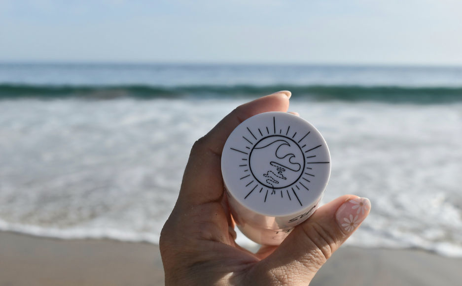 A woman is holding a Sun Stick container showing the Tides 2 Trails logo.