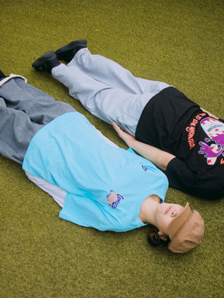 Two dancers lying on grass in the MUTE x LOVEURJAM mint blue and black tees