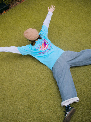 Dancer lying on grass with arms outstretched in the mint blue MUTE x LOVEURJAM tee