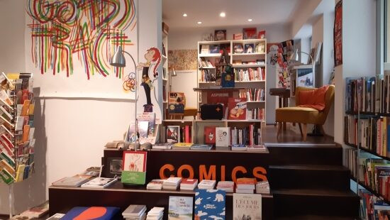 Interior shot of Zadig Buchhandlung bookshop. In the foreground is a selection of comic books on a display table, around the room are floor to ceiling bookshelves and display racks