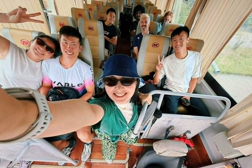 Smiling friends take a bus selfie inside a beige coach with KJ logos on seats, making peace signs.
