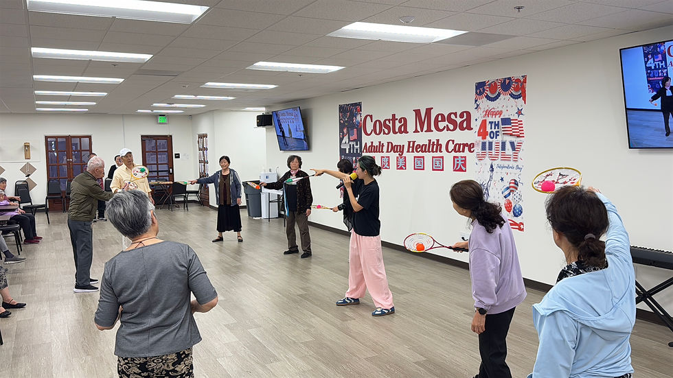 Seniors exercise in a room with wooden floors at Costa Mesa Adult Day Health Care. 4th of July decor on walls, flowball rackets in hand.