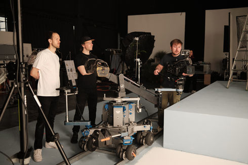 Three film crew members with camera on track dolly in studio.