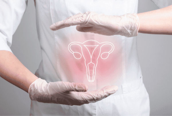 Person in white coat and gloves holds hands around glowing uterus illustration on pink background, suggesting medical care or fertility.