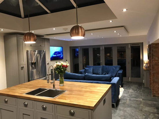 Restoration shows internal house with kitchen with island and wood worktops, stone floor lit at night