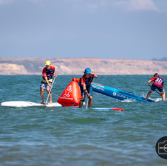 a senic view of a sup race with three paddlers roudning a red triangle race marker