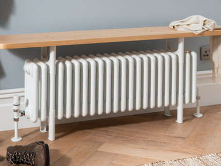 A white bench seated radiator on a wooden floor set against an eggshell colour wall
