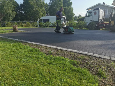 Arbeider kompakterer ny asfalt med vals på parkeringsplass.