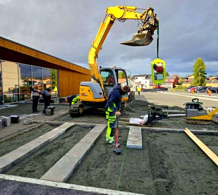 Gul gravemaskin og arbeider legger belegningsstein på Kiwi Skreia.