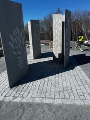 Moderne minneskulptur med grå plater og bladmotiv på brostein.