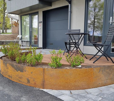 Moderne hus med rustfarget plantekasse, garasjedør og uteplass foran.