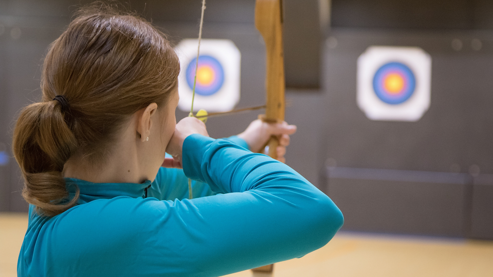 Woman taking aim at target with bow & arrow