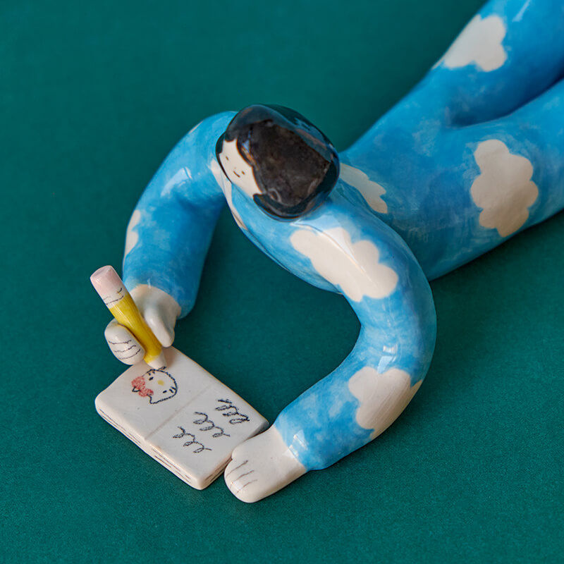 Ceramic sculpture depicting a girl writing in a journal.