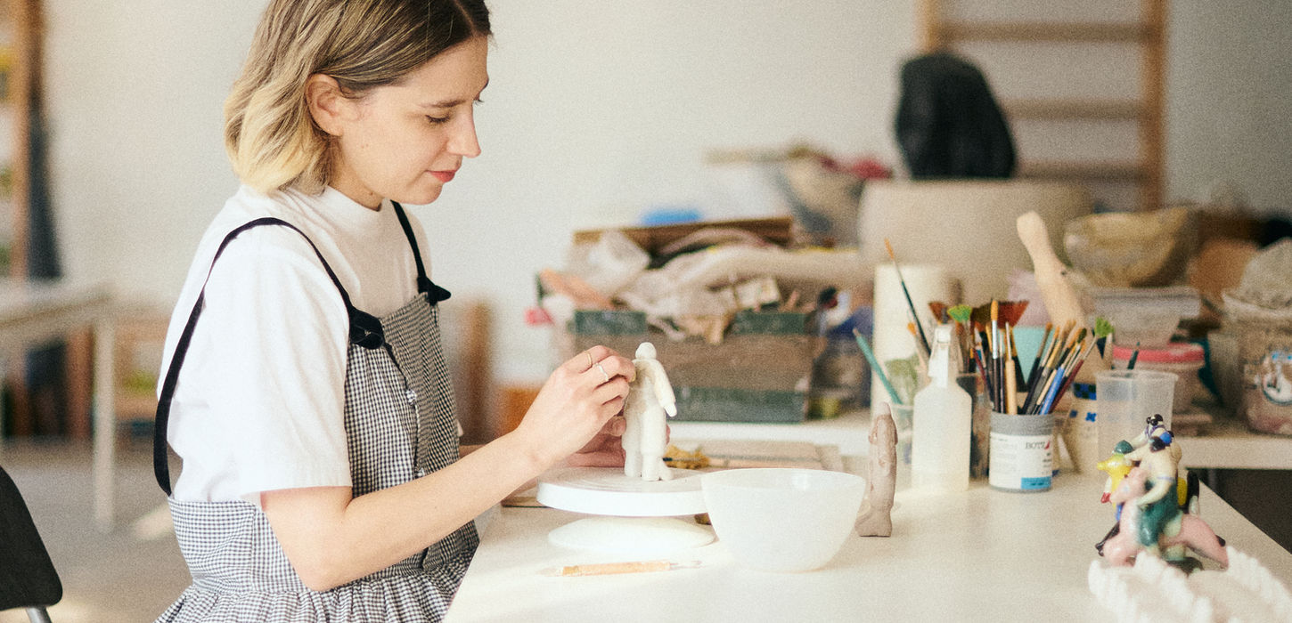 Woman in apron sculpting clay in a light-filled studio