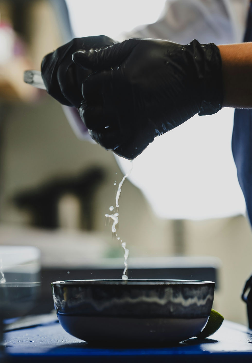 Chef squeezing liquid into a bowl while wearing black gloves. Fine Dining.