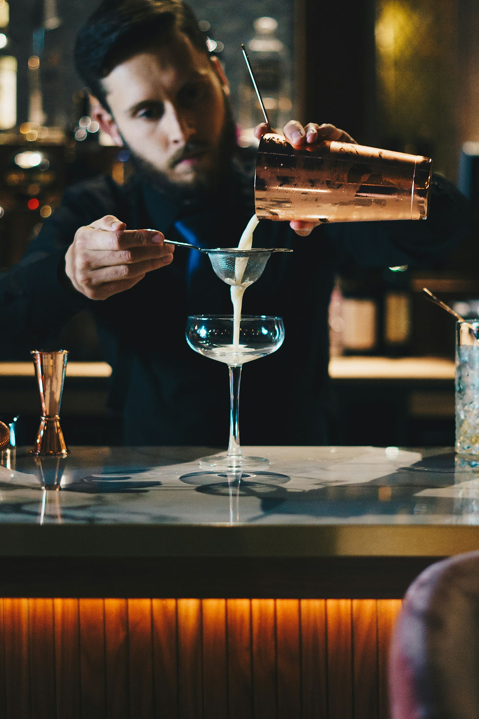 Barman schenkt cocktail in coupeglas.