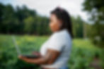 Black woman with dreadlocks typing on laptop in green field.