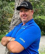 AG Snow & Stump - photo of Aaron in blue t-shirt and logo baseball hat standing in front of a tree.