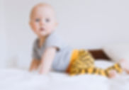 Bébé à quatre pattes sur un lit,portant un sarouel imprimé Jaune de la marque Koh mabby et un body gris simple regardant l'objectif