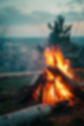 Campfire burning on a hillside overlooking a city at dusk